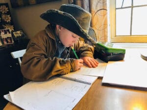 Student in a cowboy hat working at a table on school work